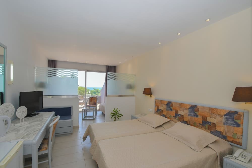 A cozy hotel room with twin beds, a colorful headboard, and a balcony overlooking the sea offers a serene retreat for travelers seeking relaxation.