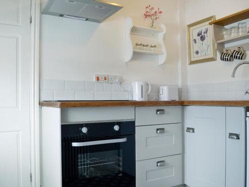 A cozy, well-lit kitchen with white cabinetry, wooden countertops, and a built-in oven exudes a homely charm, perfect for travelers seeking a comfortable self-catering accommodation.