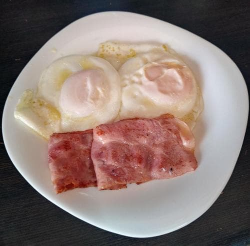 A simple breakfast plate featuring poached eggs and ham slices on a dark table evokes a cozy morning vibe, ideal for travelers seeking quick and nutritious meals during their journey.