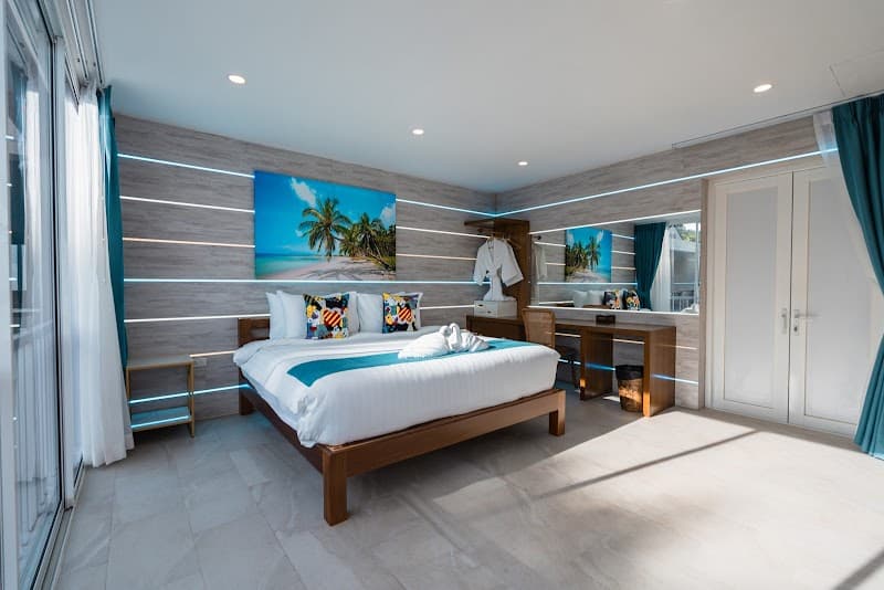 A serene and modern bedroom at LOVE Beach Club Koh Samui features a cozy bed adorned with vibrant pillows, tropical artwork, and sleek wooden furnishings, ideal for travelers seeking relaxation in a stylish coastal retreat.