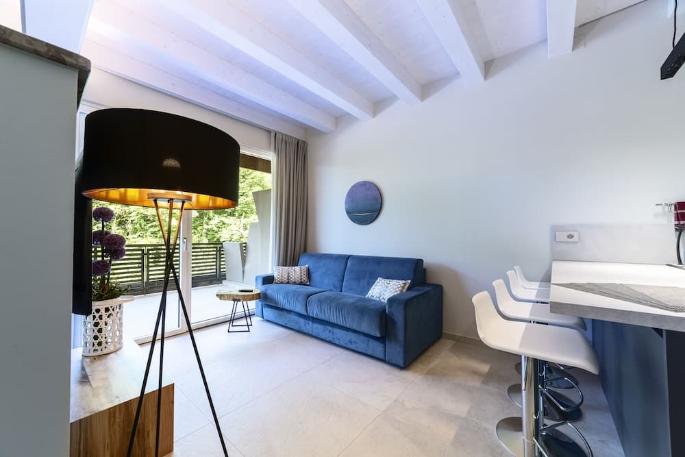 A cozy modern living space with a blue sofa, sleek bar stools, and a large window overlooking greenery, ideal for travelers seeking a tranquil and stylish vacation rental.