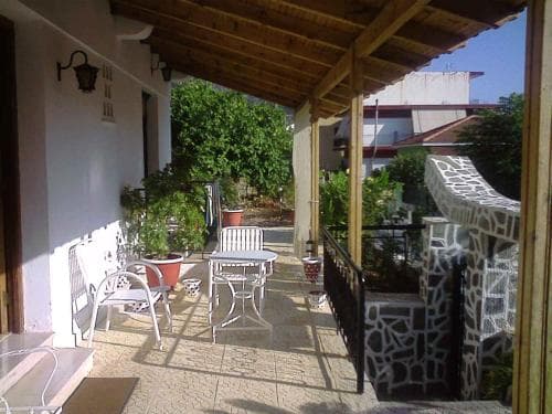 A cozy outdoor patio with white furniture, potted plants, and mosaic railings invites relaxation in a sunny residential area, perfect for travelers seeking a peaceful retreat.