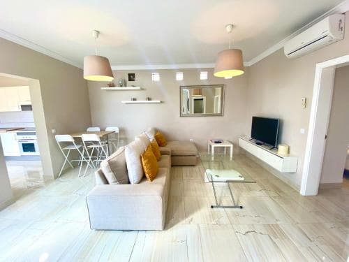 A cozy, modern apartment living room with light wood flooring, neutral-toned furniture, and warm lighting creates an inviting atmosphere, ideal for travelers seeking comfort and style in their accommodations.