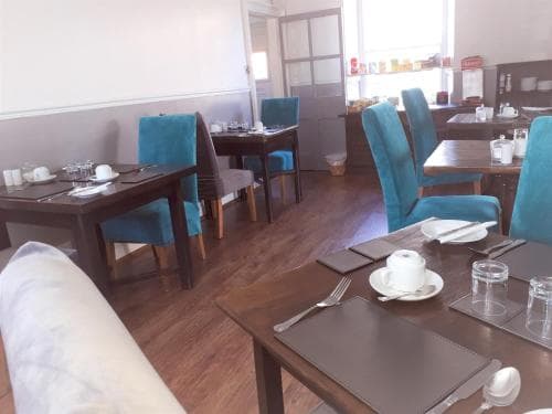 A cozy café with wooden tables, teal chairs, and neatly set tableware invites travelers to enjoy a quiet meal in a warm and inviting atmosphere.