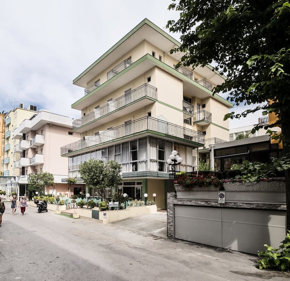 A serene street scene featuring a charming multi-story hotel with balconies, lush greenery, and pedestrians, ideal for travelers seeking a cozy urban retreat.