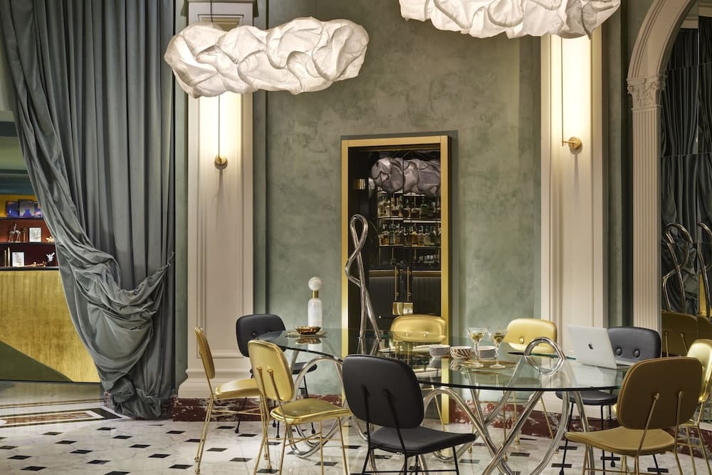 An elegant hotel lounge features luxurious gold and black chairs around glass tables under cloud-like pendant lights, set against a backdrop of plush curtains and a sophisticated bar area, ideal for travelers seeking a refined meeting or relaxation spot.