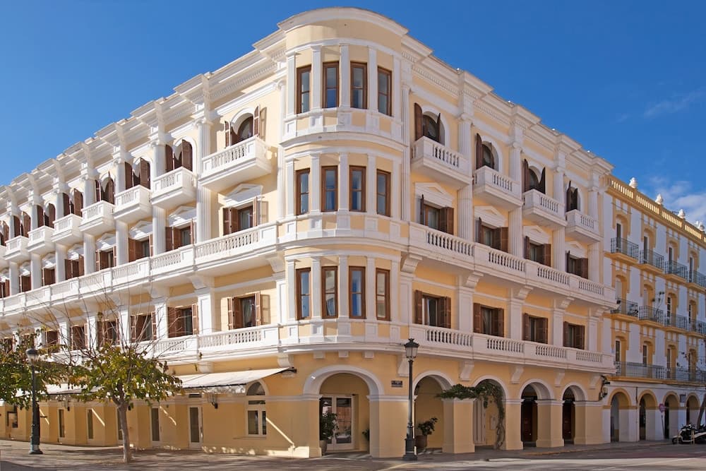 A charming European cityscape features elegant yellow and white neoclassical buildings with arched doorways and balconies under a clear blue sky, ideal for cultural exploration and leisurely strolls.