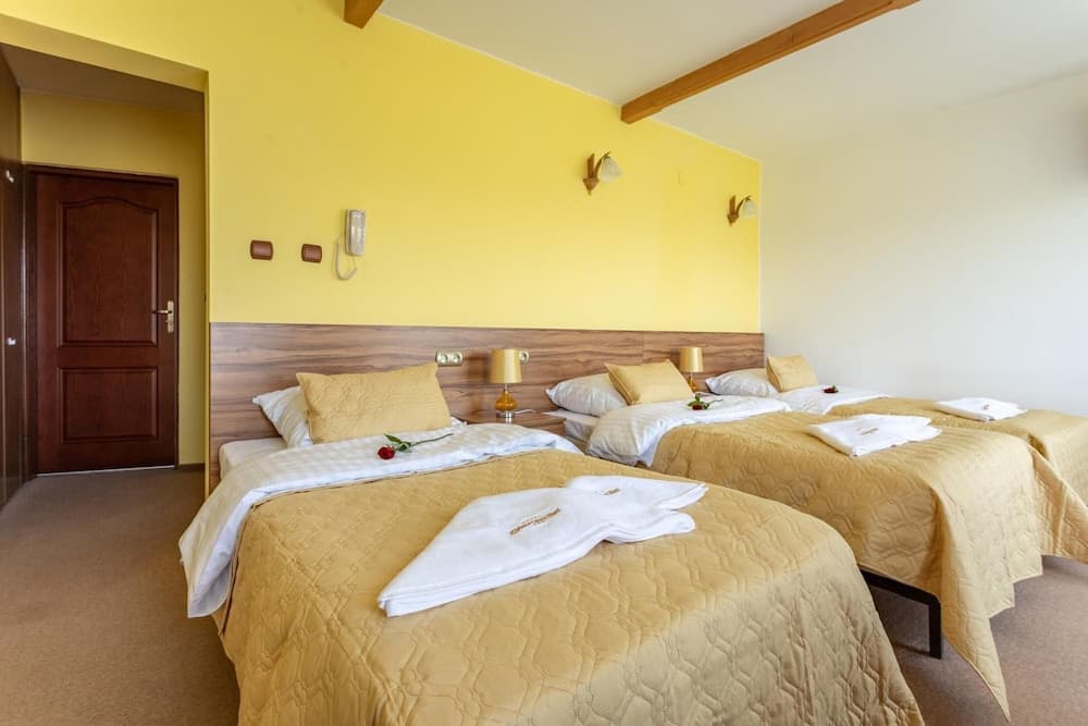 A cozy hotel room with warm yellow walls, neatly arranged twin beds adorned with fresh towels and red roses, wooden accents, and ambient lighting creates an inviting atmosphere perfect for travelers seeking comfort and relaxation.