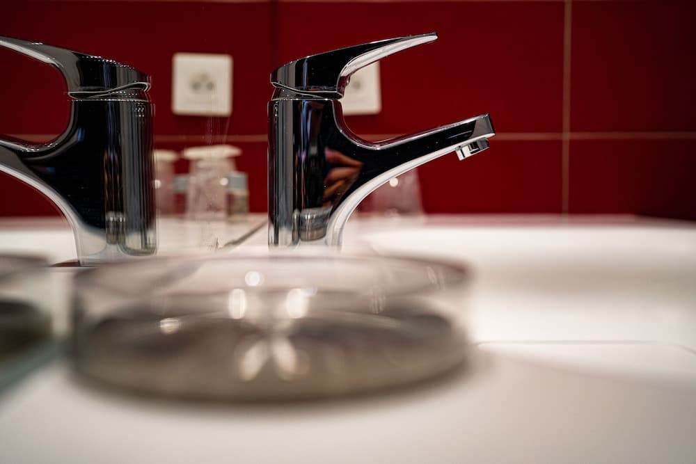 A sleek modern faucet gleams against a bold red tiled backdrop in a stylish bathroom setting, ideal for travelers seeking contemporary design elements in their accommodations.