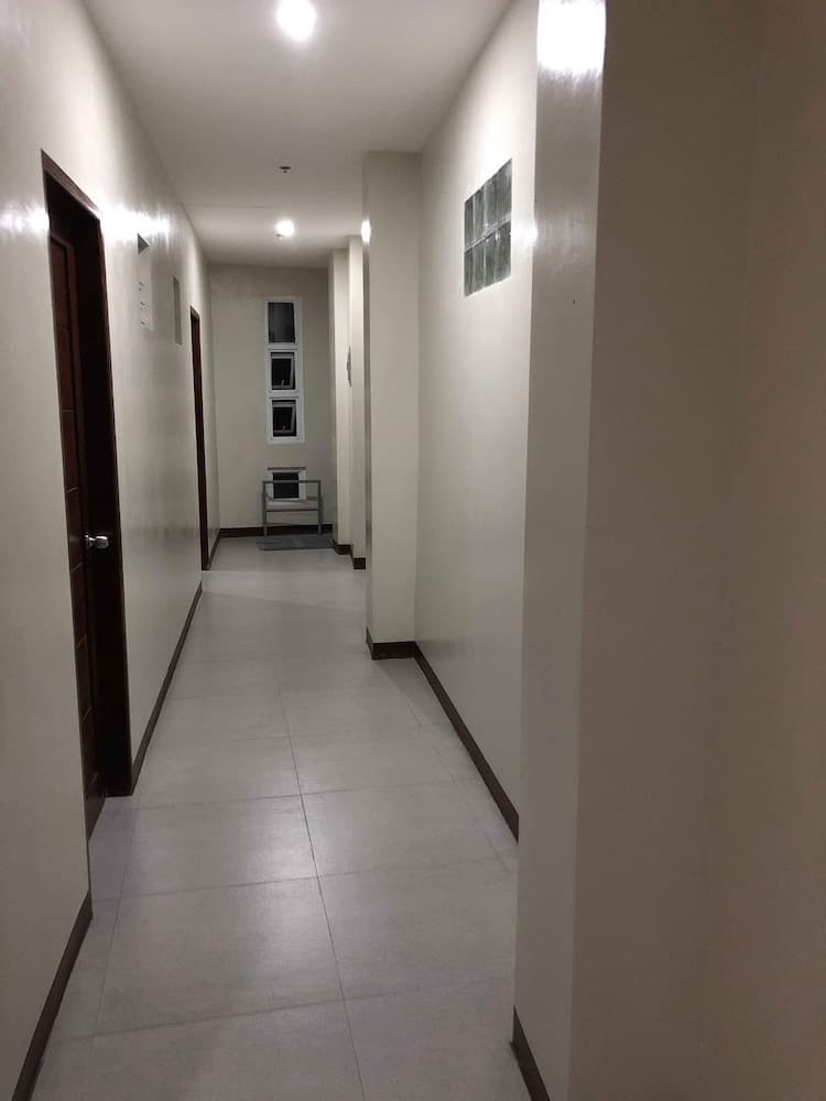 A well-lit, minimalist hotel corridor with white walls, tiled floors, wooden doors, and small windows creates a clean and serene atmosphere ideal for travelers seeking simplicity and functionality.