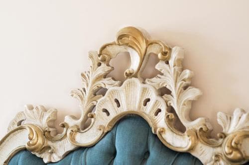 An ornate, gold-accented Rococo-style headboard against a soft beige wall exudes elegance, perfect for travelers seeking luxurious accommodations in boutique hotels or historic villas.