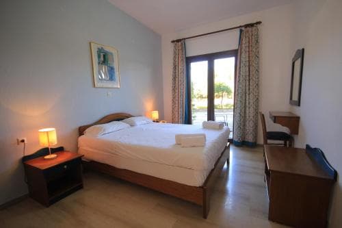 A cozy hotel room with a neatly made bed, wooden furniture, and a view of greenery through glass doors, ideal for travelers seeking comfort and relaxation.