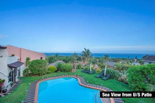 A serene coastal villa offers breathtaking sea views from its upper-story patio, featuring a sparkling pool, lush greenery, and palm trees, ideal for luxury vacation retreats.