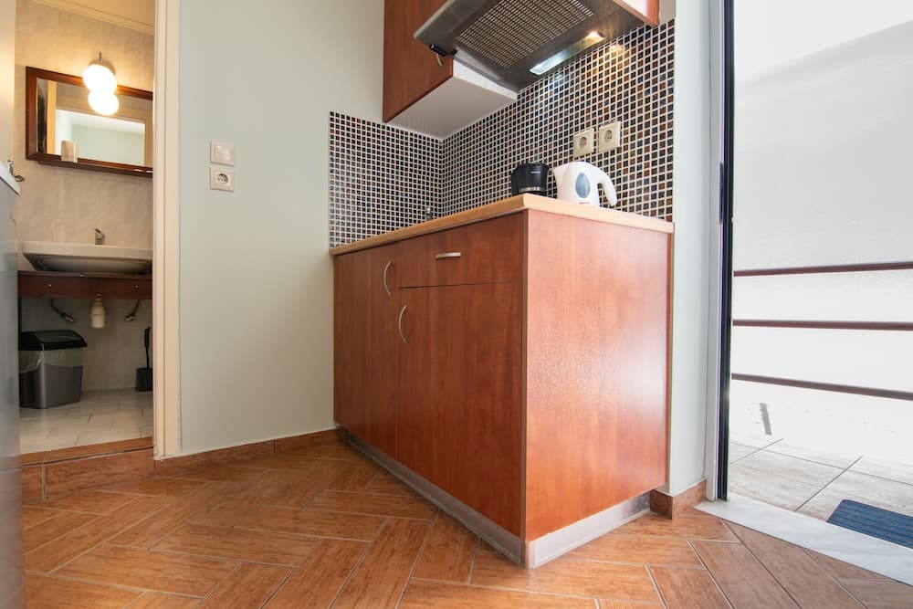 A cozy apartment kitchenette with wooden cabinets, mosaic tiles, and a view of the bathroom through an open doorway, ideal for travelers seeking compact living spaces.