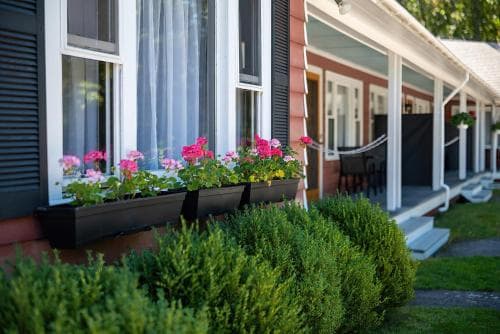 A charming cottage with vibrant flower boxes and lush greenery evokes a serene, welcoming atmosphere ideal for a relaxing getaway.