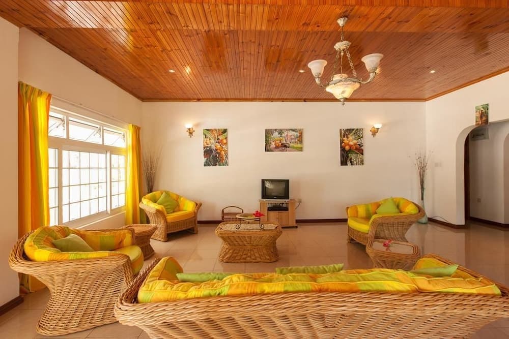 A cozy tropical living room with wicker furniture, vibrant yellow cushions, wooden ceilings, and bright artwork creates a warm and inviting atmosphere ideal for a relaxing vacation retreat.