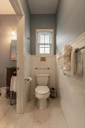 A cozy bathroom with white marble tiles, soft blue walls, neatly hung towels, and a small window offers a serene retreat, ideal for travelers seeking comfort and cleanliness in their accommodations.