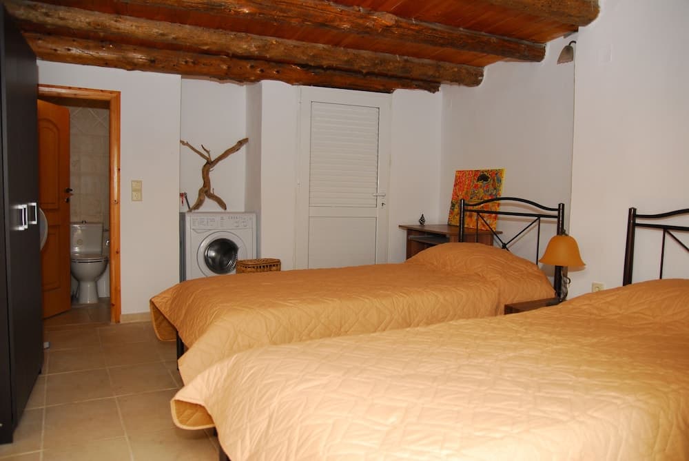 A cozy bedroom with rustic wooden beams, two neatly made beds, a washing machine, and an adjacent bathroom offers a charming retreat for travelers seeking comfort in a quaint setting.