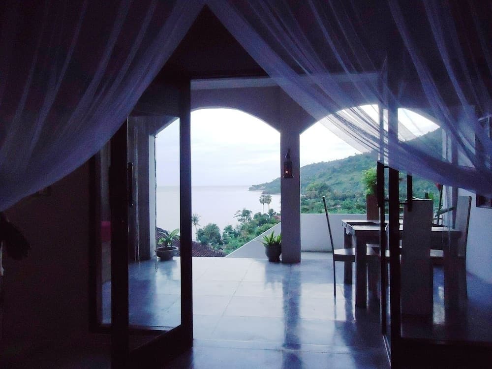 A serene balcony draped in sheer curtains offers a tranquil view of the ocean and lush greenery, ideal for a peaceful retreat or romantic getaway.