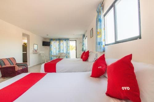 A cozy hotel room with bright red OYO pillows, colorful curtains, and natural light streaming through large windows, ideal for travelers seeking comfort and convenience.
