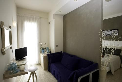 A cozy modern studio apartment features a navy blue sofa, sleek furniture, and soft natural light from a large window, creating an inviting atmosphere ideal for travelers seeking comfort and style in urban accommodations.