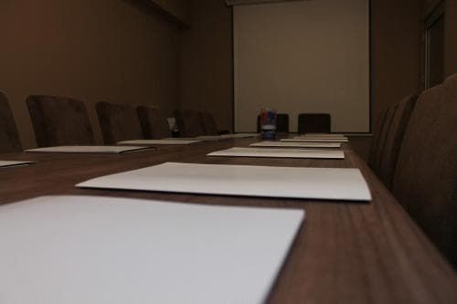 A modern conference room with a long wooden table set up for a meeting, featuring neatly arranged papers and chairs, evokes a professional atmosphere ideal for business travelers seeking venues for corporate discussions.