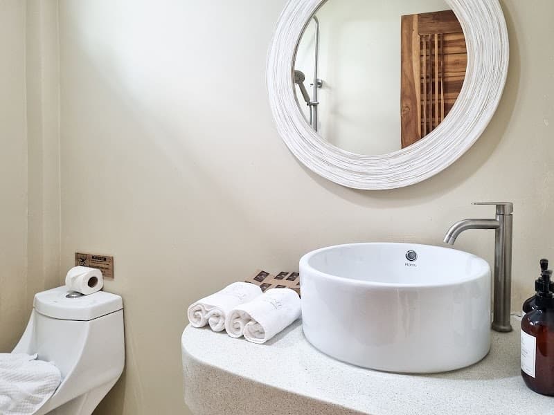 A serene bathroom at Elephant Beach Club & Resort Samui features a modern sink, round mirror, neatly folded towels, and a minimalist design, ideal for travelers seeking a tranquil and stylish accommodation experience.