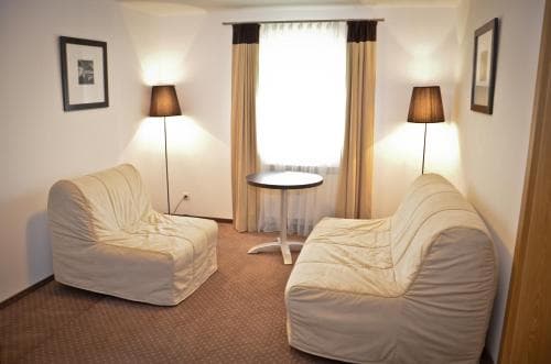 A cozy hotel room features beige armchairs, a small table by the window, soft lighting from lamps, and framed artwork, creating a serene atmosphere ideal for relaxation during a business trip.
