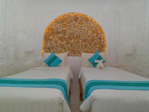 A cozy twin-bed room with a rustic stone archway exudes tranquility, perfect for travelers seeking a serene retreat in a boutique hotel setting.