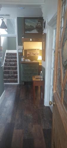 A cozy, warmly lit hallway with wooden floors, a patterned staircase, and framed artwork creates an inviting atmosphere in a quaint bed and breakfast, perfect for travelers seeking charm and comfort.