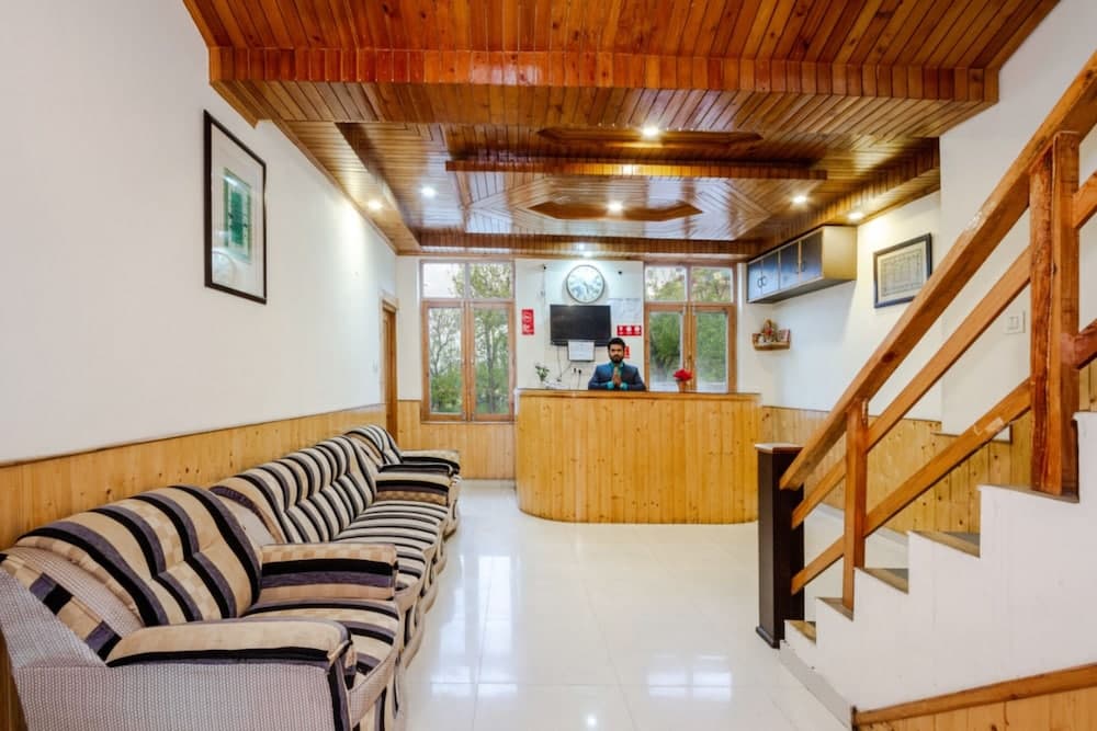 A cozy hotel lobby with wooden ceilings, striped sofas, a reception desk, and a staircase creates a welcoming atmosphere ideal for travelers seeking comfort and relaxation.