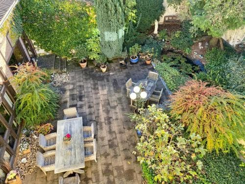 An inviting outdoor patio surrounded by lush greenery and vibrant foliage offers a serene retreat, complete with cozy seating areas and a tranquil pond, perfect for a relaxing getaway or a peaceful vacation spot.