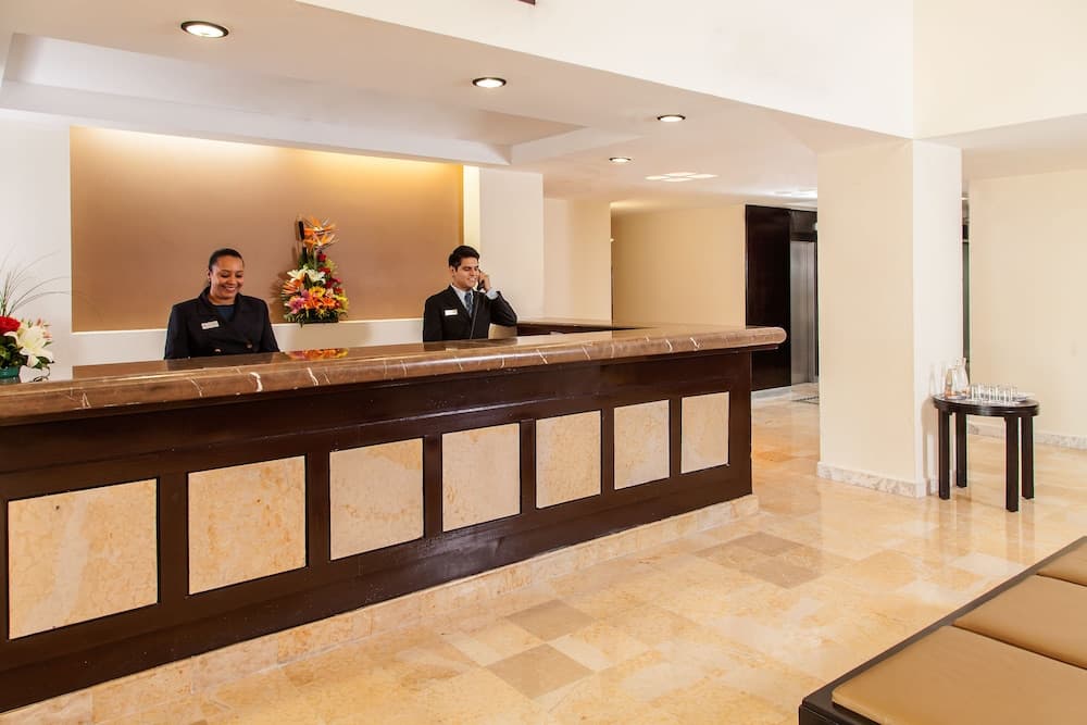 A warmly lit hotel lobby features a polished reception desk with attentive staff, vibrant floral arrangements, and a cozy seating area, ideal for travelers seeking a welcoming and professional check-in experience.
