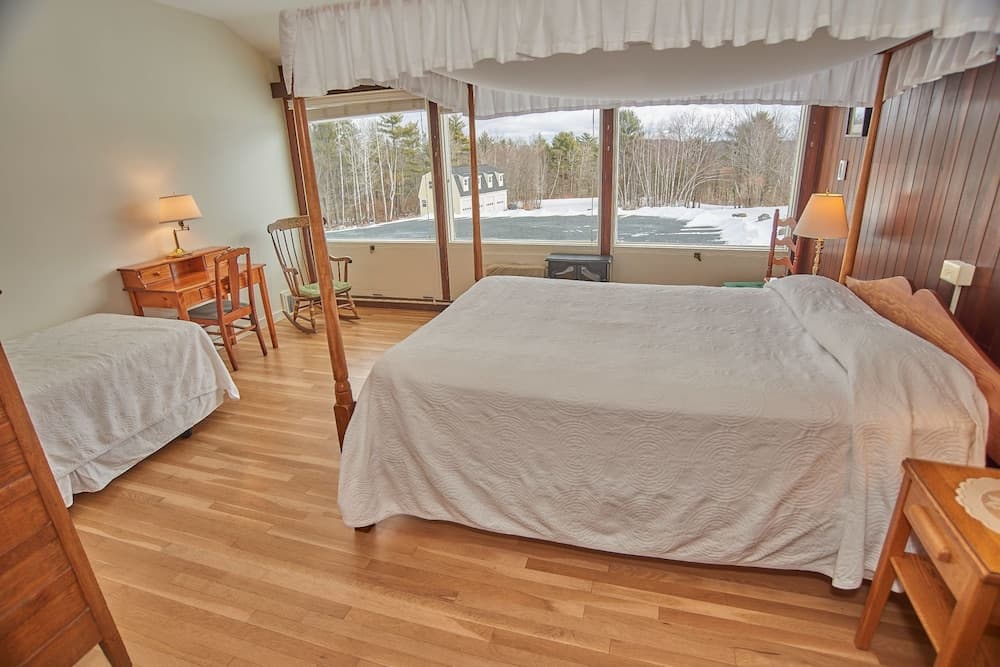 A cozy cabin bedroom with wooden floors, a four-poster bed, and large windows offering a serene winter forest view, ideal for a tranquil getaway.