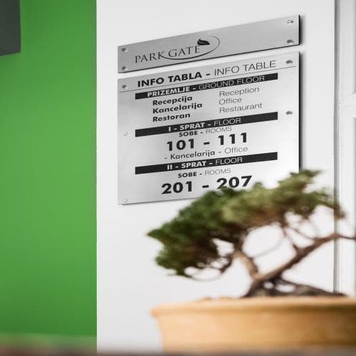 A modern hotel directory sign at Park Gate lists room numbers and amenities against a vibrant green wall, complemented by a serene bonsai tree, ideal for travelers seeking quick navigation and a tranquil atmosphere.