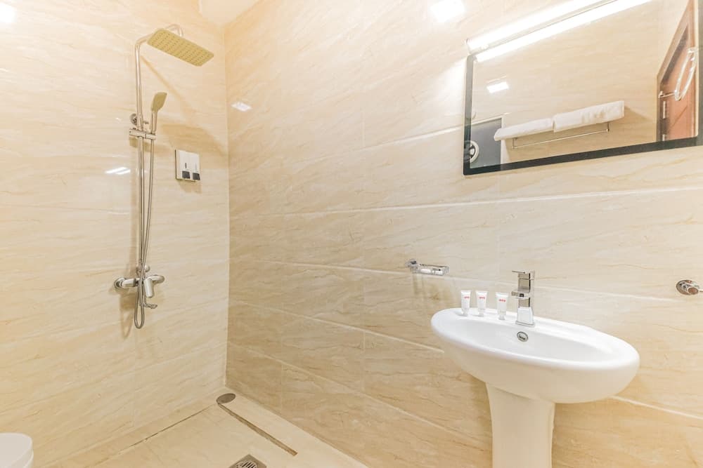 A clean, modern bathroom with beige marble tiles, a sleek shower setup, a white pedestal sink, and a mirror with ambient lighting creates a serene atmosphere ideal for travelers seeking comfort and hygiene in their accommodations.