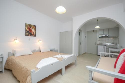 A cozy, well-lit studio apartment features a neatly made bed, vibrant artwork, and an open kitchen area, ideal for travelers seeking comfort and convenience in a compact living space.