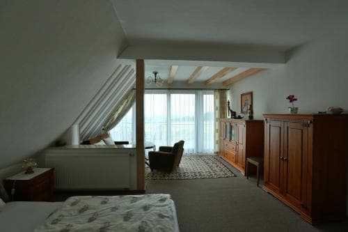 A cozy attic bedroom with slanted ceilings, wooden furniture, and large windows overlooking a serene landscape, ideal for a tranquil getaway.