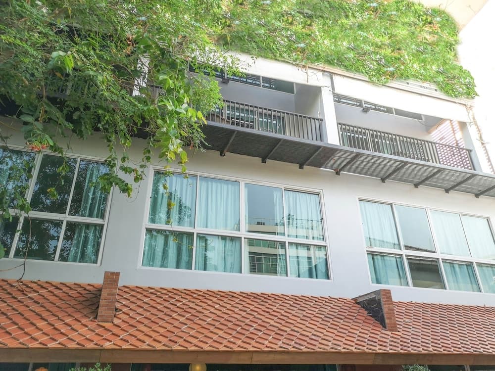 A serene urban retreat features a modern building with lush greenery spilling over balconies, large windows with sheer curtains, and a terracotta-tiled roof, ideal for travelers seeking a peaceful city stay.