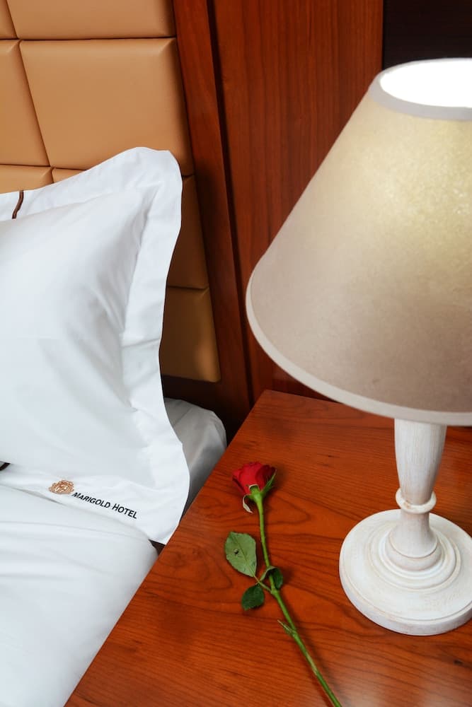 A cozy hotel room bedside scene featuring a warmly lit lamp, a single red rose on the nightstand, and plush pillows branded "Marigold Hotel," ideal for travelers seeking comfort and romance.