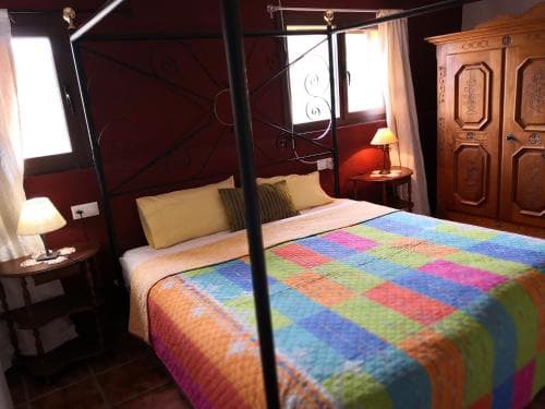 A cozy bedroom with a vibrant quilted bedspread, wooden furnishings, and soft lighting creates an inviting atmosphere ideal for travelers seeking a warm and comfortable stay in a rustic setting.