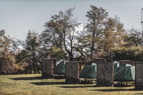A serene camping site features cozy tents nestled among lush greenery with a majestic snow-capped mountain backdrop, ideal for adventure seekers looking to connect with nature.