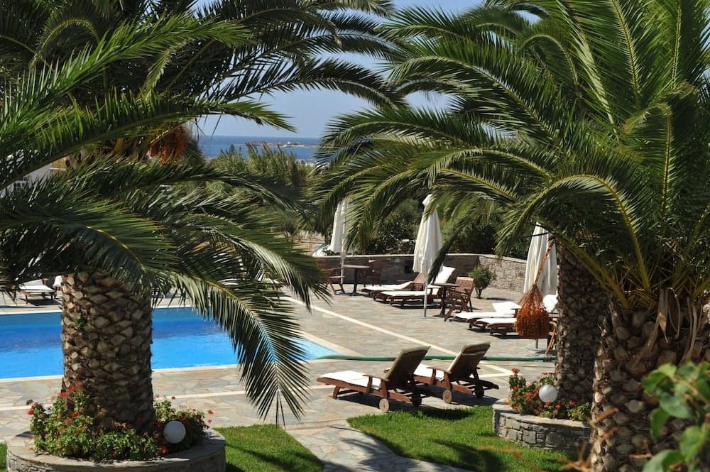 A serene tropical resort scene features lush palm trees framing a tranquil poolside area with lounge chairs and umbrellas, ideal for relaxing vacations near the sea.