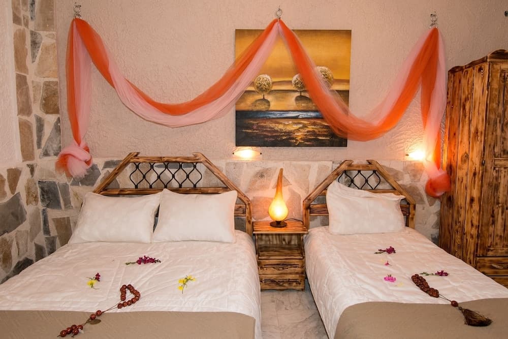 A cozy bedroom with twin beds adorned with flower petals, warm orange drapery, and rustic wooden furnishings creates an inviting atmosphere perfect for a romantic getaway.