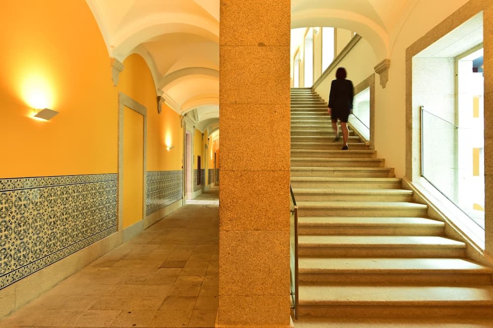 A warmly lit hallway adorned with intricate blue tiles transitions into a bright staircase where a solitary figure ascends, ideal for exploring historic architecture and capturing the serene ambiance of cultural landmarks.