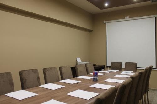 A professional meeting room features a long table set with papers and a water bottle, surrounded by chairs under warm lighting, ideal for business travelers seeking conference facilities.