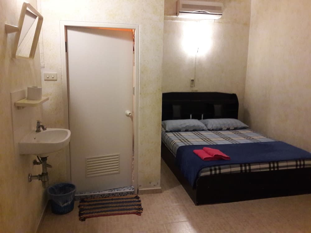 A cozy budget-friendly hotel room features a neatly made bed with plaid bedding, an attached sink area, and warm lighting, ideal for solo travelers seeking comfort in a compact space.