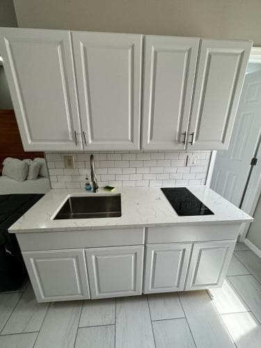 A modern kitchenette with white cabinetry, marble countertops, and a sleek black cooktop offers a clean and inviting space ideal for travelers seeking a cozy apartment rental experience.