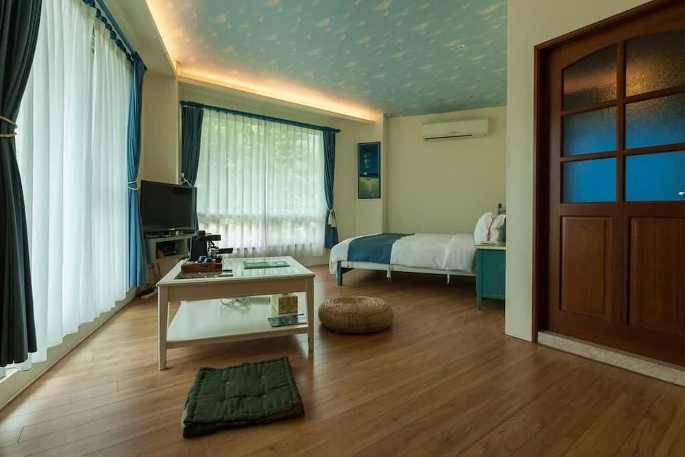 A serene hotel room with wooden floors, starry ceiling, large windows, and cozy furnishings invites travelers seeking relaxation and comfort.