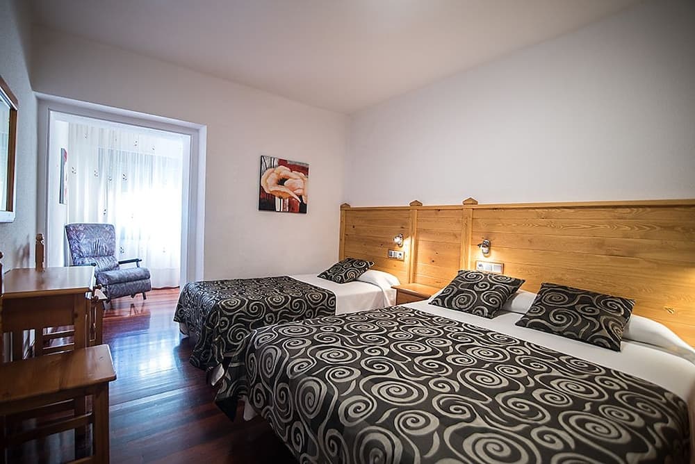 A cozy hotel room features two neatly made beds with patterned bedding, wooden furnishings, and soft natural light filtering through sheer curtains, ideal for travelers seeking comfort and relaxation.